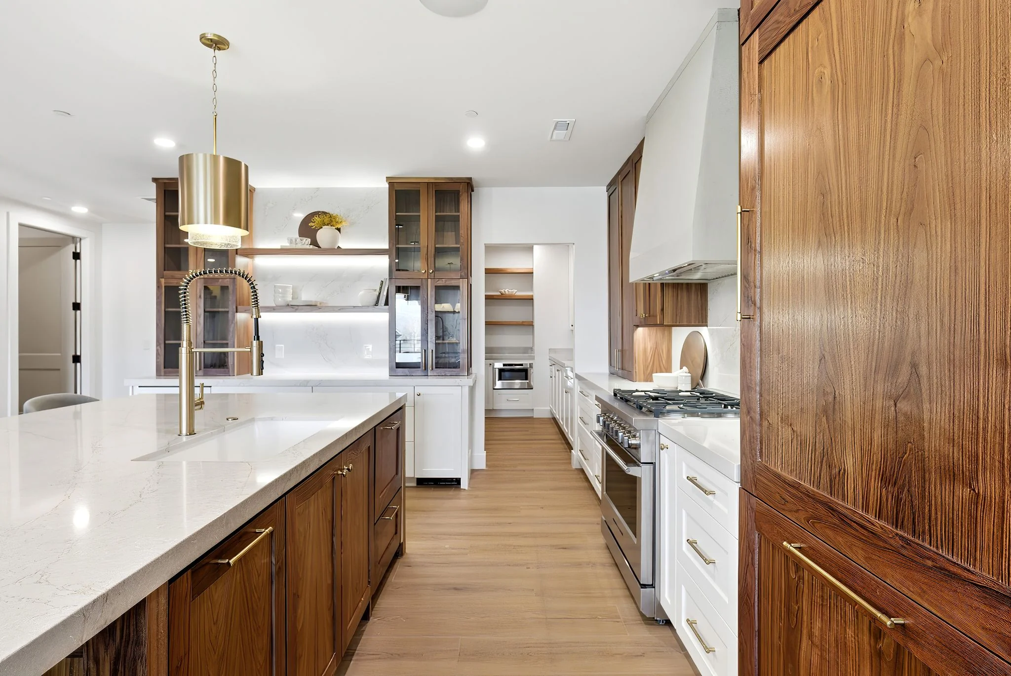 Model unit kitchen with walnut cabinetry, brass hardware, and waterfall island